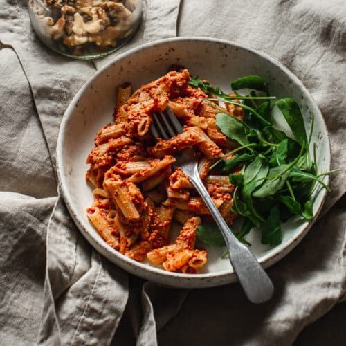 roasted cherry tomato pasta with walnuts in a bowl with a side of baby arugula