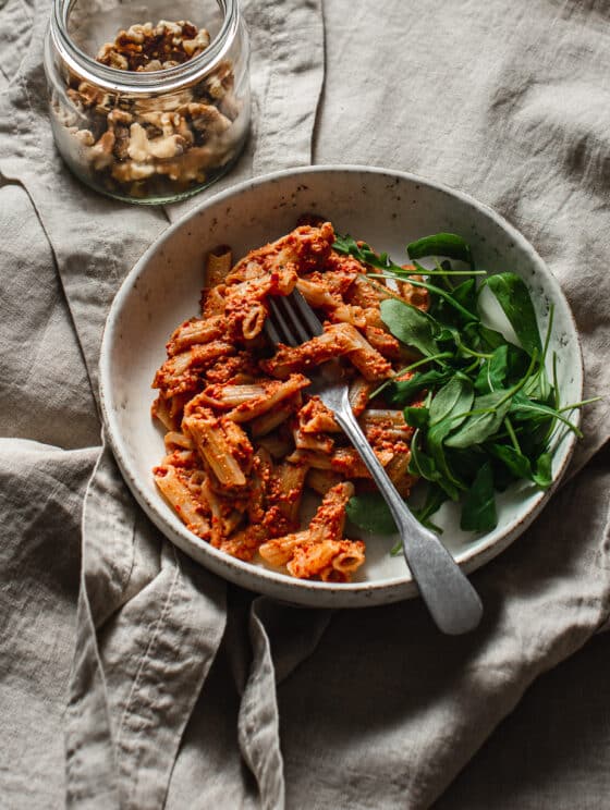 roasted cherry tomato pasta with walnuts in a bowl with a side of baby arugula